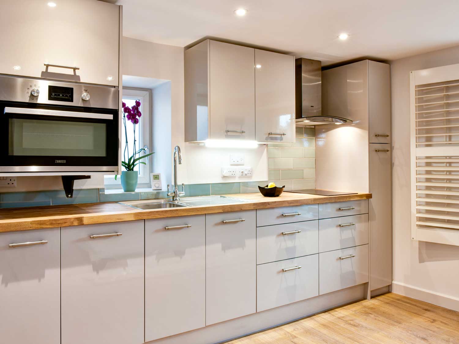 A smart, brightly lit kitchen with solid oak work surfaces and oak floor along with white kitchen units