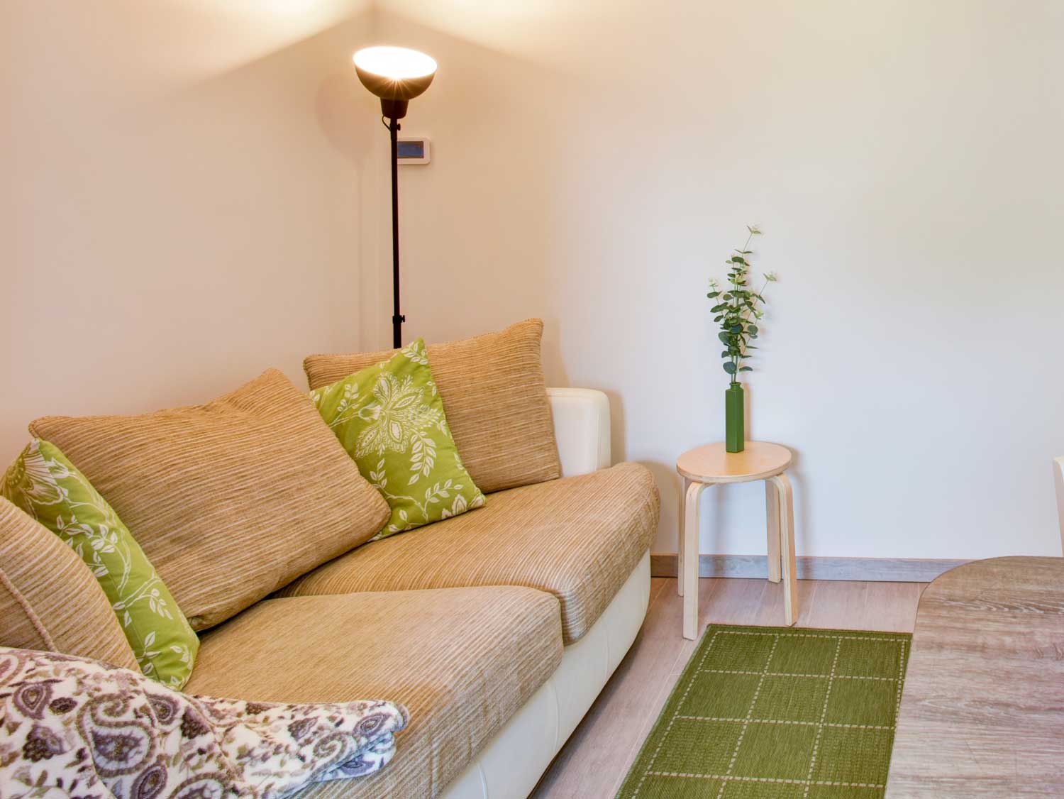 The living room in one of the apartments showing a comfortable sofa and a standard lamp in a clean, tidy and contemporary space.