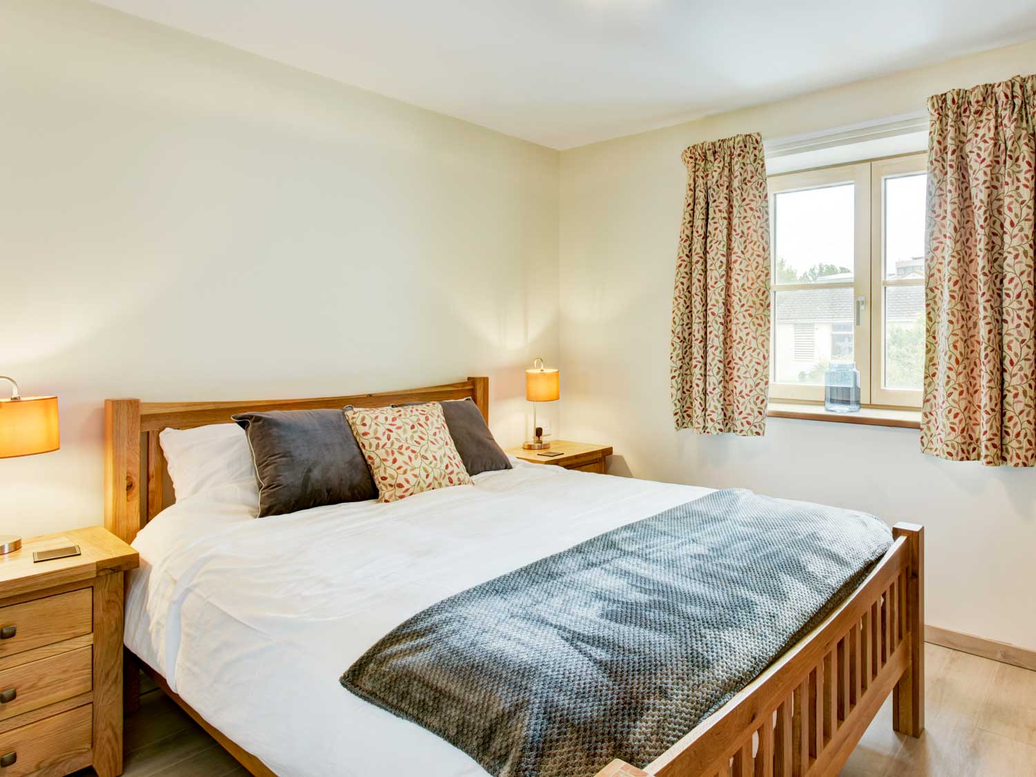 A generously sized double bedroom with double bed dressed in white bed linen and coordinating blanket and cushions.