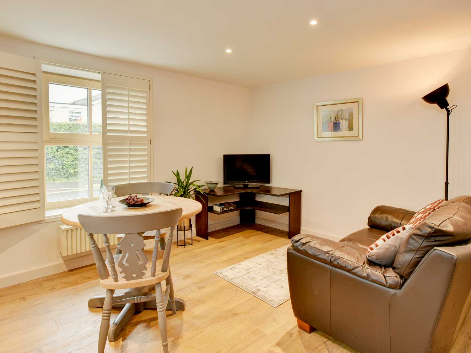 The living room in one of the apartments showing a leather recliner facing a television and window with shutters.